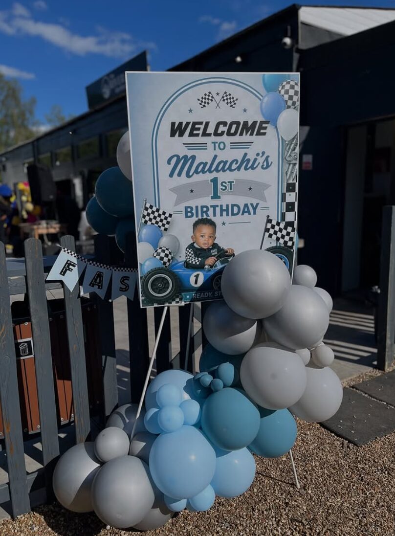 Blue and grey balloon display with a personalised first birthday welcome sign