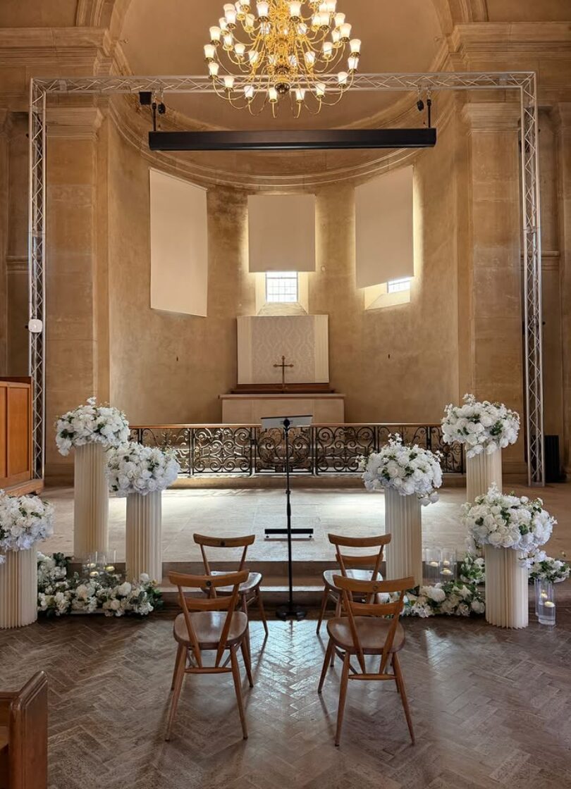 Ceremony aisle styled with white floral arrangements on fluted plinths and candles