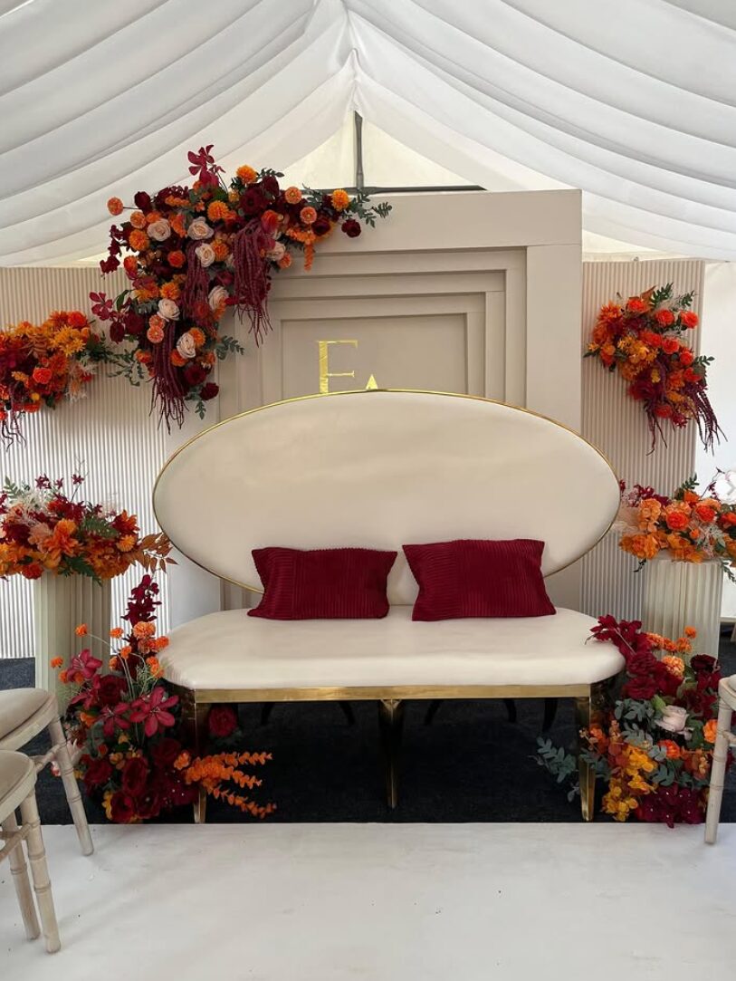 Ivory loveseat stage set with red and orange floral installation and gold detailing